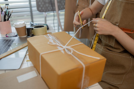 a beautiful woman fashion shop owner is live-streaming to chat with customers and pack her products into doxes to prepare for shipping to customers, parcel, tailor, designerの写真素材