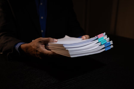 a businessman works overtime is his accounting firm's office until late at night, an entrepreneur remains at his export company because he has a lot of customer documents to checkの写真素材