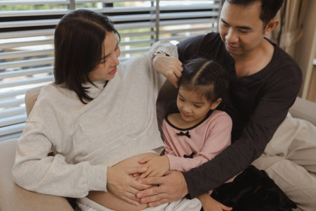 lovely family spend time together in their house, a pregnant mother sits on the couch with her...