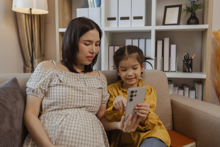 a pregnant mother spent a weekend with her daughter, they did a lot of activities together on the sofa in the living room, family, enjoyment, parent, mother and daughterの写真素材