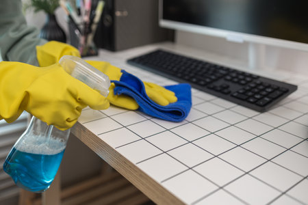 a company's cleaning lady is diligently cleaning the executive's office, the cleaning lady wears rubber gloves to prevent irritation form chemicals while cleaningの写真素材