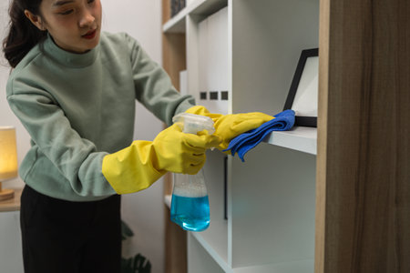 the wife is cleaning her husband home office, cleanup the room, wearing rubber glove to protect her hands, tidy upの写真素材