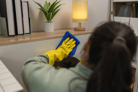 the wife is cleaning her husband home office, cleanup the room, wearing rubber glove to protect her...