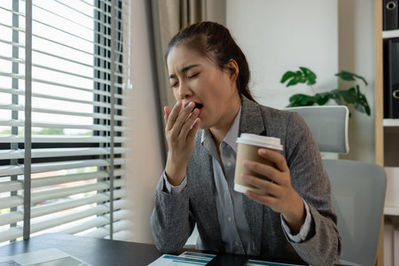 a female employee is feeling very stressed and tired form work, a businesswoman shows signs of extreme fatigue because she has been editing important documents from morning till night, overtimeの写真素材