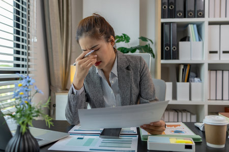 a female employee is feeling very stressed and tired form work, a businesswoman shows signs of extreme fatigue because she has been editing important documents from morning till night, overtimeの写真素材