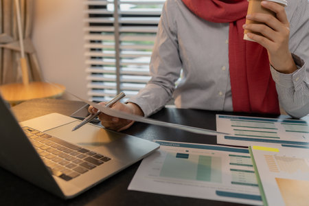a muslim female employee is working on financial and accounting documents at a company in her private office, hijab, marketing, the female muslim company president is sitting in her office workingの写真素材