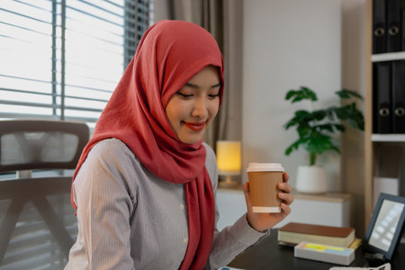 a muslim female employee is working on financial and accounting documents at a company in her private office, hijab, marketing, the female muslim company president is sitting in her office workingの写真素材