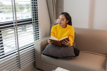 a woman is spending her holiday in the living room of her house, feeling peaceful and happy because she has done many activities that make her feel relaxed, lifestyle, apartment, sofa, couchの写真素材
