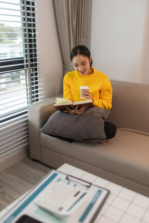 a woman is spending her holiday in the living room of her house, feeling peaceful and happy because she has done many activities that make her feel relaxed, lifestyle, apartment, sofa, couchの写真素材