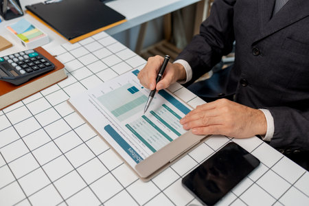 a businessman is sitting at work in his private office, an employee is handling documents to finish on time, accountant, finance, statistics documents, professional, workplaceの写真素材