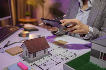 an experienced female engineer is giving a final check to a house model in her private office to make sure it meets the blueprints and meets the construction deadlineの写真素材