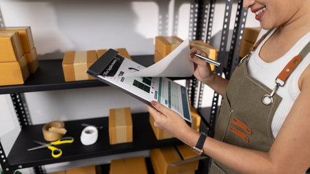 a female employee is checking parcel boxes in a warehouse, a warehouse manager is counting parcel boxes on shelves, a small online business owner is in a storage roomの写真素材