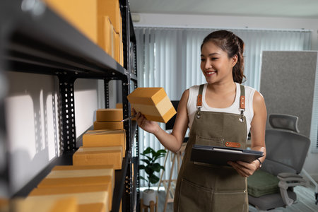 a female employee is checking parcel boxes in a warehouse, a warehouse manager is counting parcel boxes on shelves, a small online business owner is in a storage roomの写真素材
