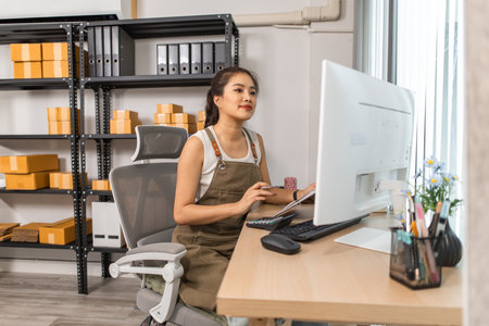 warehouse manager is entering data into computer, an employee is checking shipping addresses for accuracy in the stockroom, a small business owner is working in an online business warehouseの写真素材
