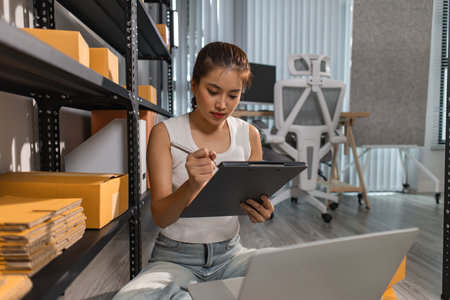 a female employee is checking parcel boxes in a warehouse, a warehouse manager is counting parcel boxes on shelves, a small online business owner is in a storage roomの写真素材