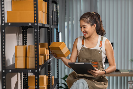 a female employee is checking parcel boxes in a warehouse, a warehouse manager is counting parcel boxes on shelves, a small online business owner is in a storage roomの写真素材