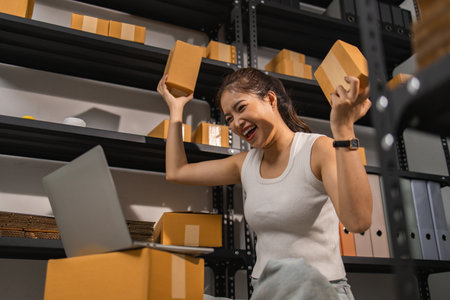 a small online business owner is feeling very happy because her business is successful, the entrepreneur shows her joy while she is in her warehouse, parcel, small business, joyfulの写真素材