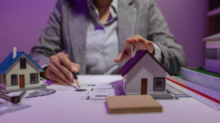 an experienced female engineer is giving a final check to a house model in her private office to make sure it meets the blueprints and meets the construction deadlineの写真素材
