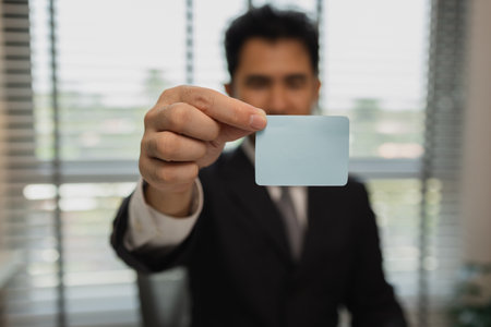 a businessman holds a small piece of paper and hands it forward, a office worker holds a blank piece of paper in his hand, a businessman holds a small piece of paper in the office, copy spaceの写真素材