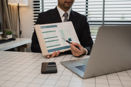 a businessman is studying information in a document to gain a better understanding, a department head is reviewing statistical documents sent by his subordinates, accountant, officeの写真素材