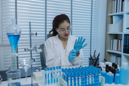 a female scientist is working in lab, a chemist tests liquid sample in science laboratory, she wears a lab coat when she works in laboratory, test tube, scientific equipmentの写真素材