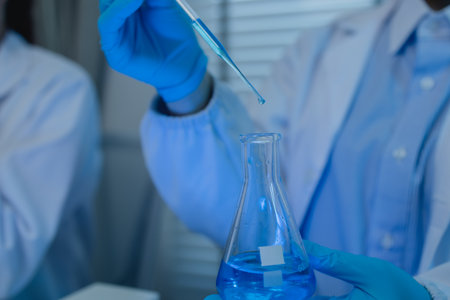 when in a lab, scientists wear lab coats, rubber gloves, and safety goggles, two chemists are testing chemicals in a liquid state, chemists working in a laboratoryの写真素材