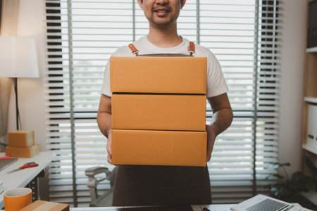 he holds a parcel box and looks at the camera, a packing staff holds a parcel box ready for delivery, an online business owner is in his office, small business, product, online, e-businessの写真素材