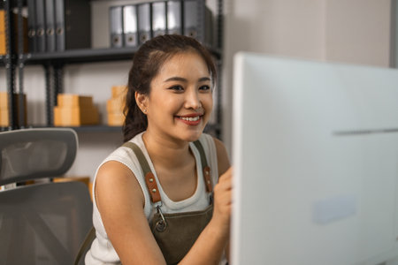 warehouse manager is entering data into computer, an employee is checking shipping addresses for accuracy in the stockroom, a small business owner is working in an online business warehouseの写真素材