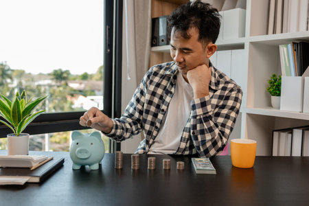 he is saving money for his future plans, putting some if his income in a piggy bank, he is saving bills and coins for emergencies, the coins are stacked on top of each other, earningの写真素材