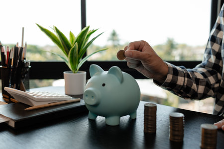 he is saving money for his future plans, putting some if his income in a piggy bank, he is saving bills and coins for emergencies, the coins are stacked on top of each other, earningの写真素材
