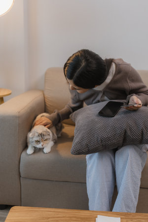 she spends her free time at home with her cat, she and her cat sit on the sofa on the weekend at the apartment, the adorable cat sits next to its owner, her pet is a lovely cat that lives in the houseの写真素材
