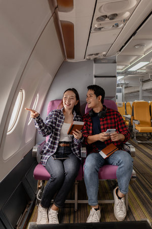 A young couple enjoys their travel experience together, smiling and chatting while sitting in airplane seats. They appear excited and connected, sharing a joyful moment before their flight departure.の写真素材
