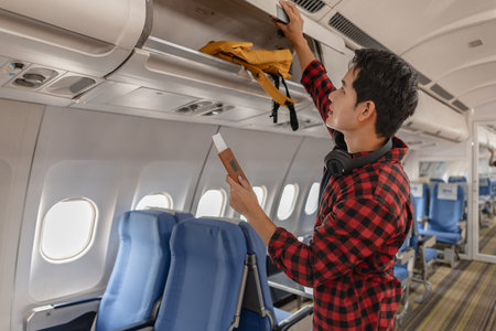 Young man preparing for a flight by placing his belongings in the overhead compartment on an...