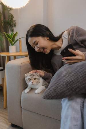 she spends her free time at home with her cat, she and her cat sit on the sofa on the weekend at the apartment, the adorable cat sits next to its owner, her pet is a lovely cat that lives in the houseの写真素材