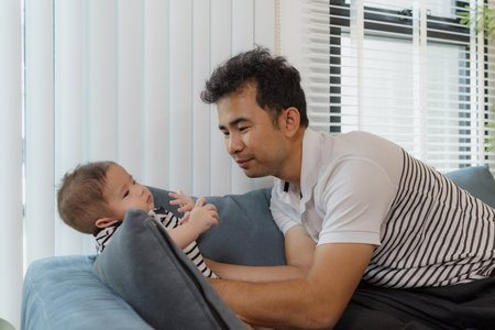 A cheerful father bonding with his baby in the living room, smiling warmly while holding the infant...