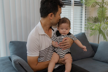 A cheerful father bonding with his baby in the living room, smiling warmly while holding the infant...