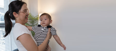 A young mother is holding her baby while spending quality time together indoors. She looks at her...
