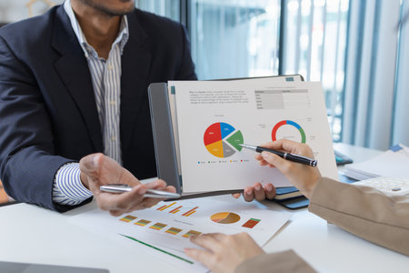 Two business professionals are discussing financial charts and strategies in a modern office. They exchange ideas, analyze reports, and negotiate solutions during a formal meeting.の写真素材
