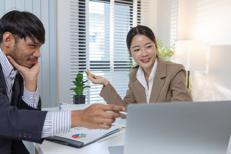 Two business professionals are discussing financial charts and strategies in a modern office. They exchange ideas, analyze reports, and negotiate solutions during a formal meeting.の写真素材
