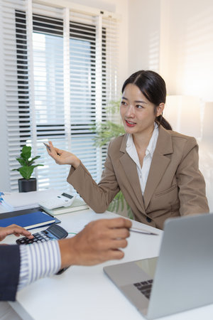 Two business professionals are discussing financial charts and strategies in a modern office. They exchange ideas, analyze reports, and negotiate solutions during a formal meeting.の写真素材