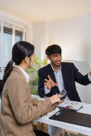Business colleagues are engaged in a collaborative discussion, analyzing financial charts and reports on the wall and table. They exchange ideas, review strategies, and plan future goals.の写真素材