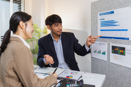 Business colleagues are engaged in a collaborative discussion, analyzing financial charts and reports on the wall and table. They exchange ideas, review strategies, and plan future goals.の写真素材