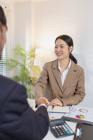 Business partners finalize their meeting with a handshake, symbolizing trust, agreement, and successful collaboration. They confirm decisions after analyzing charts and reports.の写真素材