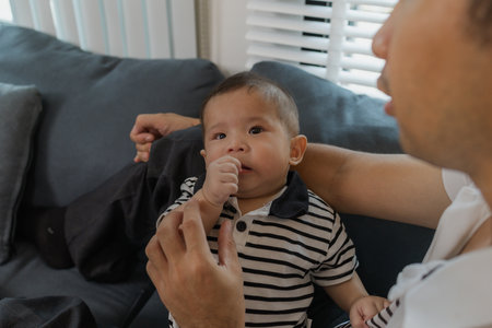 A tender moment of a father holding his baby, as the infant looks up with curiosity and trust. The...