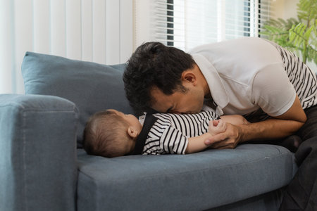 A tender moment of a father holding his baby, as the infant looks up with curiosity and trust. The warm interaction reflects family love, bonding, and parental care.の写真素材