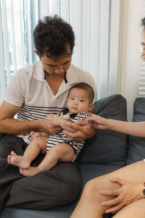 A young family shares tender moments with their baby in a cozy home. The father kisses the baby tiny...