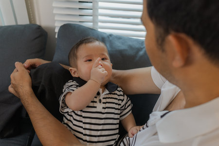 A tender moment of a father holding his baby, as the infant looks up with curiosity and trust. The warm interaction reflects family love, bonding, and parental care.の写真素材