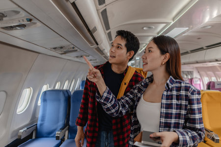 Happy couple walks through the airplane cabin, pointing and smiling as they look for their seats. Their cheerful expressions reflect the excitement of traveling together and starting their new journeyの写真素材