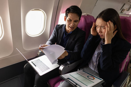 A stressful moment during a flight where a manager appears to be scolding his secretary over a work mistake. The woman looks upset and overwhelmed while holding documents in a tense discussion.の写真素材