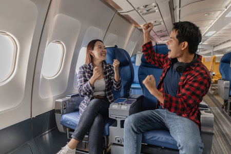 Excited couple celebrating together while sitting on an airplane. Their cheerful expressions and body language suggest joy and enthusiasm about their journey or shared travel experience.の写真素材